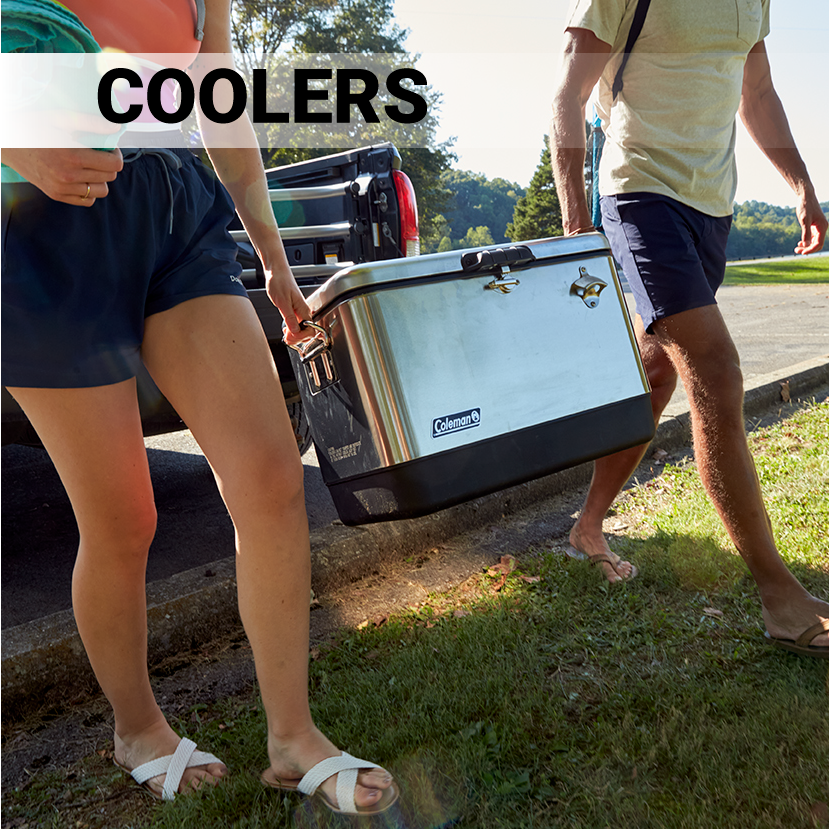 Man and woman in summer clothes carrying a stainless steel Coleman 54qt Steel Belted Cooler across gross
